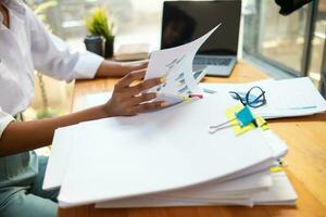 mujer de negocios manos trabajando en pilas de papel documentos a buscar y revisión documentos apilado en mesa antes de enviando ellos a tablero de directores a utilizar correcto documentos en reunión con empresario foto