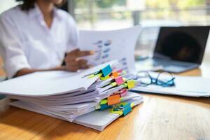 mujer de negocios manos trabajando en pilas de papel documentos a buscar y revisión documentos apilado en mesa antes de enviando ellos a tablero de directores a utilizar correcto documentos en reunión con empresario foto