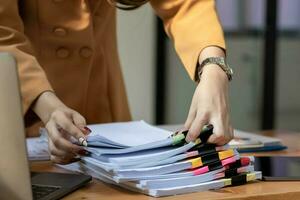 mujer de negocios manos trabajando en pilas de papel documentos a buscar y revisión documentos apilado en mesa antes de enviando ellos a tablero de directores a utilizar correcto documentos en reunión con empresario foto