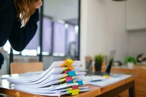 mujer de negocios manos trabajando en pilas de papel documentos a buscar y revisión documentos apilado en mesa antes de enviando ellos a tablero de directores a utilizar correcto documentos en reunión con empresario foto