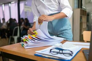 mujer de negocios manos trabajando en pilas de papel documentos a buscar y revisión documentos apilado en mesa antes de enviando ellos a tablero de directores a utilizar correcto documentos en reunión con empresario foto