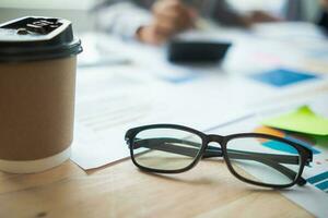 Glasses with black frames placed on a desk in office are eyeglasses that are prepared for wearing when looking at resolutions because eyeglasses will help adjust eyesight to be sharper in vision photo