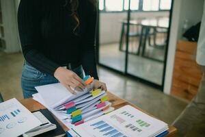 mujer de negocios manos trabajando en pilas de papel documentos a buscar y revisión documentos apilado en mesa antes de enviando ellos a tablero de directores a utilizar correcto documentos en reunión con empresario foto