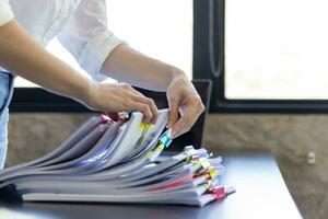 Businesswoman hands working on stacks of paper documents to search and review documents piled on table before sending them to board of directors to use  correct documents in meeting with Businessman photo