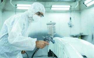 Auto mechanic in car spray room giving the spray nozzle injected into the car front bumper of the car with refinement in order to create beauty that blends with the original color of the car photo