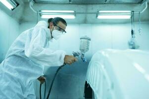 Auto mechanic in car spray room giving the spray nozzle injected into the car front bumper of the car with refinement in order to create beauty that blends with the original color of the car photo