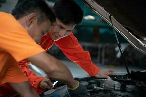 ambos de auto mecánica son inspeccionando el motor de un clientes coche siendo trajo en para reparar a un cochera. foto