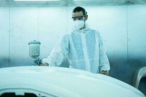 Auto mechanic in car spray room giving the spray nozzle injected into the car front bumper of the car with refinement in order to create beauty that blends with the original color of the car photo