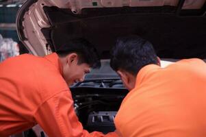 ambos de auto mecánica son inspeccionando el motor de un clientes coche siendo trajo en para reparar a un cochera. foto