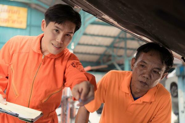 Both of auto mechanics are inspecting the engine of a customer's car being brought in for repair at a garage.