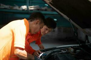 ambos de auto mecánica son inspeccionando el motor de un clientes coche siendo trajo en para reparar a un cochera. foto