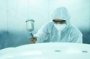 Auto mechanic in car spray room giving the spray nozzle injected into the car front bumper of the car with refinement in order to create beauty that blends with the original color of the car photo