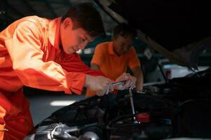 Both of auto mechanics are inspecting the engine of a customer's car being brought in for repair at a garage. photo