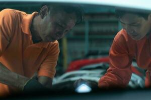 Both of auto mechanics are inspecting the engine of a customer's car being brought in for repair at a garage. photo