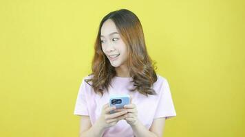 Asian woman talking mobile phone in cute pink shirt looking various promo on yellow background video