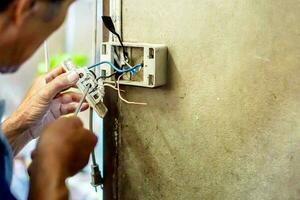 de cerca eléctrico reparar técnico participación destornillador y fijación el eléctrico toma de corriente en antiguo edificio pared. foto