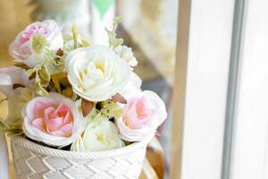 Decorate white and pink fabric roses in white plastic basket placed by the window in coffee shop. photo