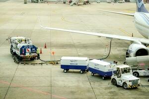 Bangkok, Thailand 2018 - New gen airline ground staff refueling the airplane and using cargo cart delivery baggage to loader cart loading luggage to the airplane. photo