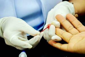 Closeup hands of nurse wear a rubber white medical gloves using capillary tube touch and drain on the blood of human ring finger to check glucose in blood at medical clinic. photo