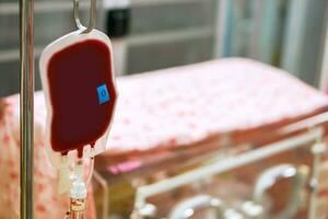 Blood in a bag hanging on a pole is transferring blood to a sick newborn baby in a baby incubator in a hospital. photo