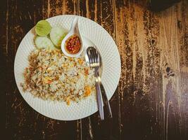 frito arroz con Cerdo en un lámina, tenedor, cuchara, y chile pescado salsa, metido en un de madera mesa foto