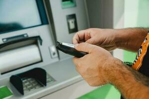 Man ATM card. ATM insert card. Man putting credit card in atm machine while holding wallet photo