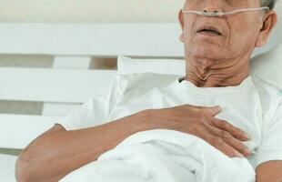 Sad senior man lying on the hospital bed and with a nasal breathing tube for treatment respiratory. Concept of Health care for the elderly, quarantine coronavirus COVID-19 photo