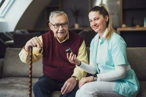 Elderly man with female caretaker at home. Health concept. photo