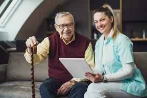 Elderly man with female caretaker at home. Health concept. photo