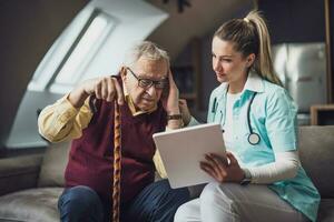 Elderly man with female caretaker at home. Health concept. photo