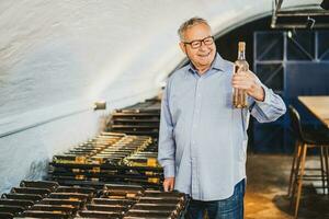 Portrait of senior man who owns winery. He is examining quality in his wine cellar. Industry wine making concept. photo
