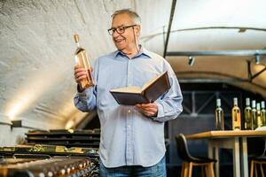 Portrait of senior man who owns winery. He is examining quality in his wine cellar. Industry wine making concept. photo