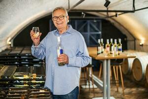 Portrait of senior man who owns winery. He is examining quality in his wine cellar. Industry wine making concept. photo