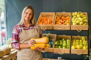 Woman works in fruits and vegetables shop. She is holding squashes. photo