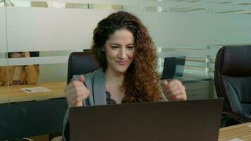 feliz mulher sentindo-me animado olhando às computador portátil tela sentado às local de trabalho ser promovido. video