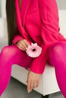 cerca arriba de un rosado gerbera flor en el manos de un joven mujer en color fucsia ropa foto