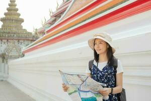 viajero, viaje joven asiático mujer o niña utilizando local mapa a Turismo a pagoda templo, ciudad turismo, contento en soleado día.mochilero turista, fiesta viaje verano o vacaciones. foto