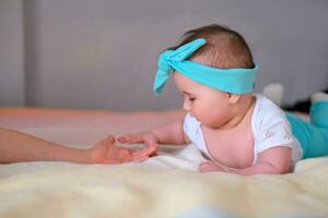 A 6-month old baby lies on his stomach on the bed and touches his sister's hand. A beautiful headband for a baby. photo