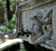antique brass drinking fountain, trickle of water, human face bas-relief, hot summer day photo