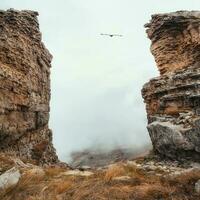 Soft focus. Dangerous gorge, a cliff between two rocks. Dramatic fog among giants rocky mountains. Ghostly atmospheric view to big cliff in cloudy sky. Low clouds and beautiful rockies. photo