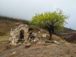 Old family crypt on a misty mountain slope. Old Erzi tower complex in the Jeyrah gorge, located on the extremity of the mountain range in Ingushetia, Russia. photo