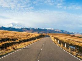 soleado autopista a el nevadas picos otoño Mañana abandonado carretera. hermosa asfalto autopista, autopista, autopista mediante de caucásico paisaje montañas sierras. foto