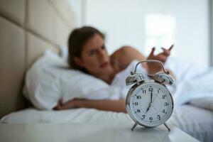 Woman lying in bed turning off an alarm clock in the morning at 5am. Hand turns off the alarm clock waking up at morning, girl turns off the alarm clock waking up in the morning from a call. photo