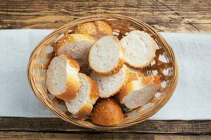 Fresh white bread, baguette slices in a wicker basket. Wooden rustic table background. Close up photo