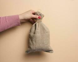 un mujer mano sostiene un lona bolso en un beige fondo, el concepto de un subvención, ayuda foto