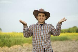 Asian man farmer is at agriculture field,wears hat, plaid shirt, pose hand lift up. Feels confident.  Concept , Agriculture occupation.Copy space of adding text or advertisement. photo