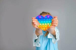 The child is holding a rainbow pop it fidget toy instead of a head.Push bubble fidget sensory toy - washable and reusable silicon stress relief toy. photo