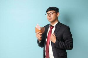 Portrait of young Asian business man in casual suit with confidence expressions fixing collar and holding leather wallet with thousand rupiahs. Isolated image on blue background photo