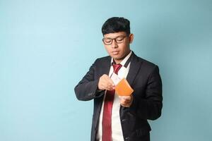 Portrait of young Asian business man in casual suit holding leather wallet and pulling out thousand rupiahs. Isolated image on blue background photo