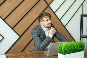 A cheerful man in a jacket sits at his desk in the office and emotionally discusses issues with a colleague photo